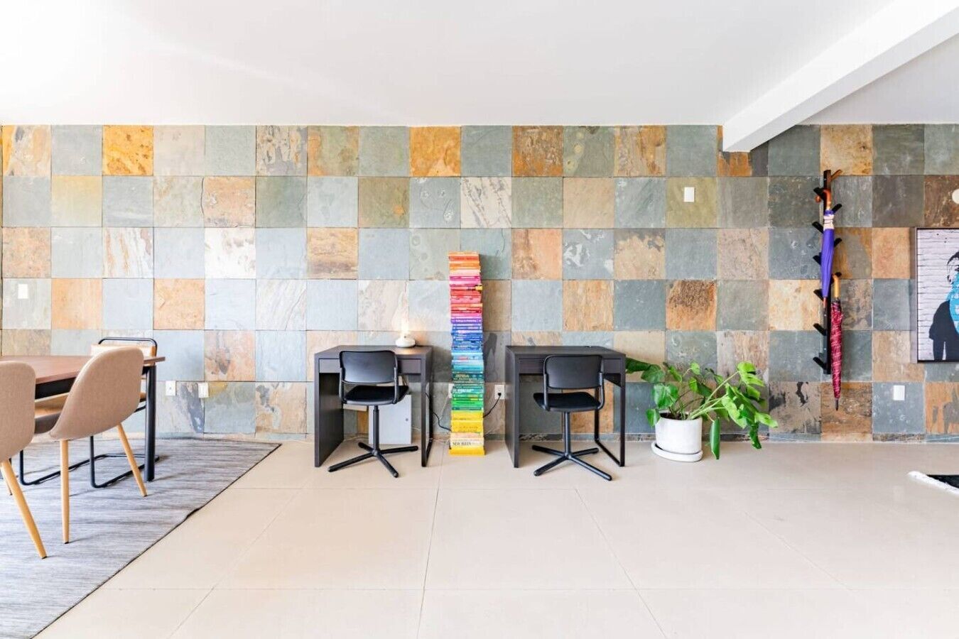 A modern office space with two desks, chairs, a potted plant, and a colorful vertical art installation.
