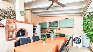 An outdoor kitchen area with a brick oven, dining table, chairs, and a ceiling fan. - Aloe Boutique Hotel Powered by Anissa Beach (Hersonissos)