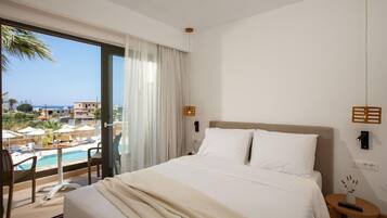 A hotel room with a large bed, a view of a pool and buildings, and a balcony with chairs.