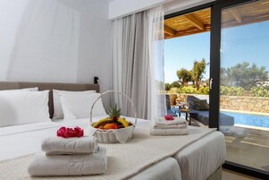 Habitación de hotel con cama, cesta de frutas, toallas y vistas a una piscina y zona exterior.