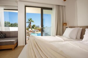 Habitación de hotel con cama, sofá, vista a una piscina y palmeras, y un balcón.