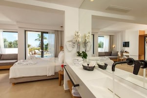 Habitación de hotel con cama, zona de estar con vistas, un espejo grande y una encimera con toallas.