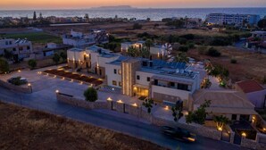 A residential area with modern houses, a parking lot, and a view of the sea at sunset. - Aloe Boutique Hotel Powered by Anissa Beach (Hersonissos)