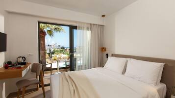 A hotel room with a bed, a desk, a chair, a TV, and a view of a pool and palm trees.