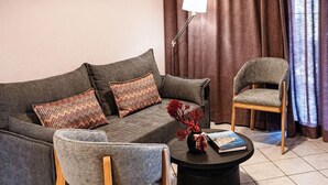 A living room with a sofa, two armchairs, a coffee table, a lamp, and a framed picture on the wall. - Aloe Boutique Hotel Powered by Anissa Beach (Hersonissos)