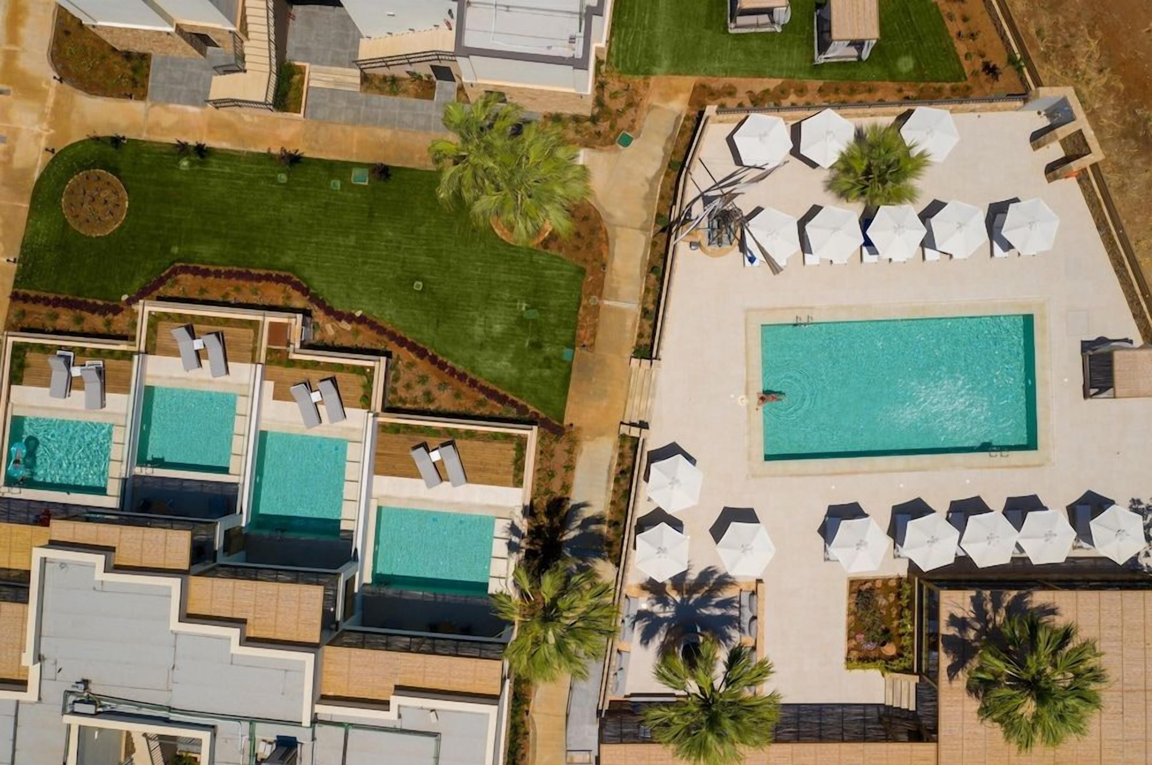 An aerial view of a resort with multiple swimming pools, lounge areas with umbrellas, and landscaped gardens.