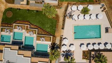 An aerial view of a resort with multiple swimming pools, lounge areas with umbrellas, and landscaped gardens.