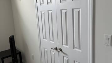 Uma porta branca fechada, com maçaneta, uma ventilação na parede e uma cadeira preta com um fio.