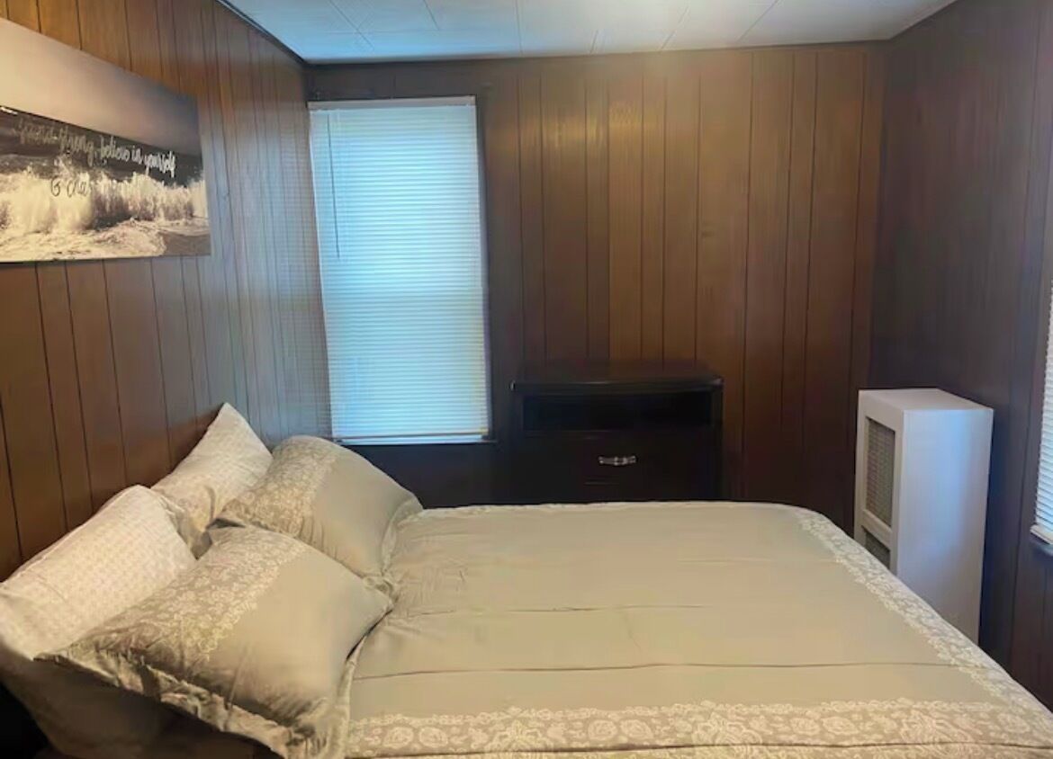 A bedroom with a bed, a dresser, a television, and a window with blinds.