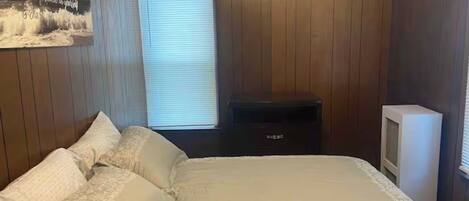 A bedroom with a bed, a dresser, a television, and a window with blinds.