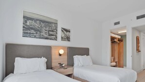 A hotel room with two beds, a nightstand with a clock, and a wall-mounted light. - Bay-View High-Rise: Priv Balcony, Pool & Gym (Miami)