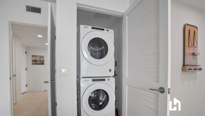 A laundry room with two stacked Whirlpool washing machines, a door with a handle, and a wall-mounted wooden rack. - Bay-View High-Rise: Private Balcony, Pool & Gym (Miami)