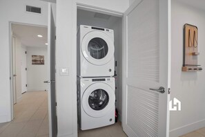 Ein Waschraum mit zwei übereinander gestapelten Whirlpool-Waschmaschinen, einer Tür mit Griff und einem an der Wand befestigten Holzregal.