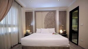 A large bed with a wooden platform, a wall-mounted artwork, and a mirror. - Cairo Taj Dokki Families Tower Hotel (Giza)