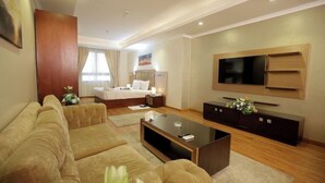 A modern hotel room with a sofa, a flat-screen TV, a bed with a headboard, and a bedside table. - Cairo Taj Dokki Families Tower Hotel (Giza)