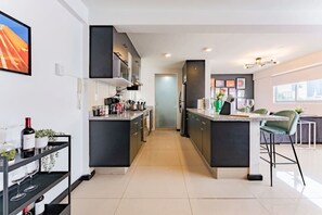 A modern kitchen with dark cabinetry, a central island, and a dining area with a bar stool. - Artful Roma Norte Stay Near Museums & Cafés (Cuauhtemoc)
