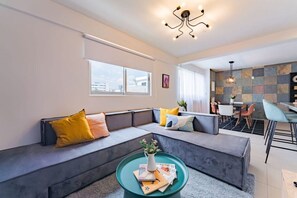 A modern living room with a sectional sofa, a coffee table with magazines, and a dining area with chairs and a table. - Artful Roma Norte Stay Near Museums & Cafés (Cuauhtemoc)