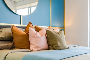 Un lit avec plusieurs oreillers de différentes couleurs et un miroir rond accroché au mur.