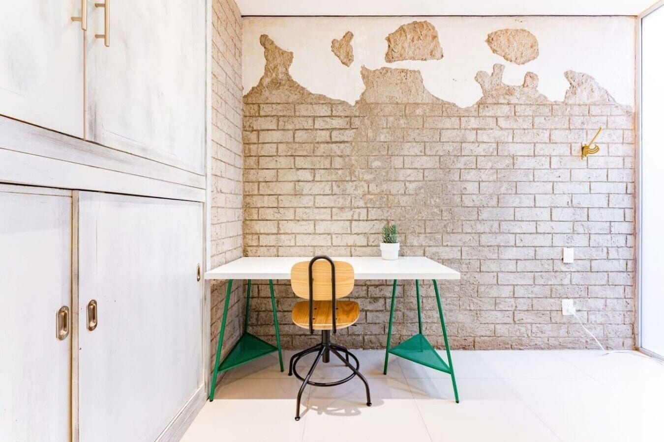A room with a white table, a chair, a small plant, and a brick wall with exposed brickwork.