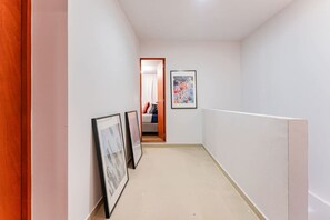 A narrow hallway with white walls, a wooden door on the left, and a bed visible through an open door at the end. - Penthouse in Roma Norte with City Skyline View (Mexico City)