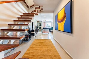 Un intérieur moderne avec un escalier en bois, une grande peinture abstraite et un espace de vie comprenant un canapé et des fauteuils.