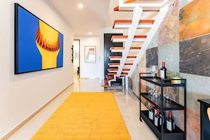 A modern interior with a yellow carpet, a staircase with wooden steps, and a wine rack with bottles. - Penthouse in Roma Norte with City Skyline View (Mexico City)