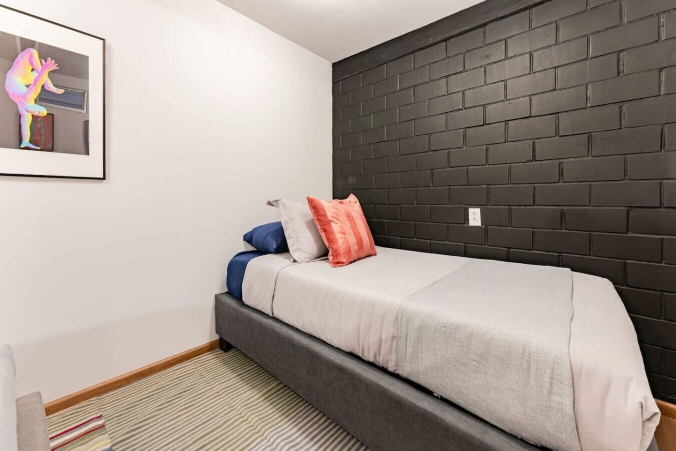 Une chambre à coucher avec un lit, des oreillers, une œuvre d’art murale et un mur en briques noires.