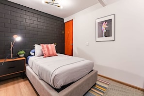 A modern bedroom with a bed, bedside table, lamp, and a framed picture on the wall. - Penthouse in Roma Norte with City Skyline View (Mexico City)