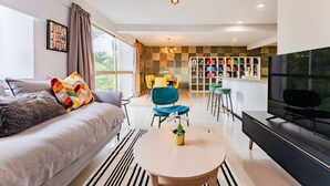 En moderne stue med sofa, rundt sofabord, fjernsyn og et køkkenområde med bar og stole.