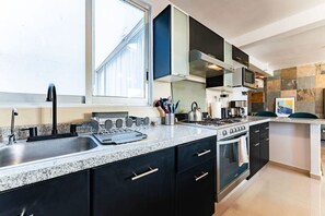 A modern kitchen with a double sink, stove, oven, and black cabinets. - Penthouse in Roma Norte with City Skyline View (Mexico City)