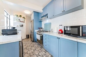 A modern kitchen with blue cabinets, a stainless steel refrigerator, a red blender, and a patterned floor. - Vibrant Condo in Roma Norte Walk to Museums & Eats (Mexico City)