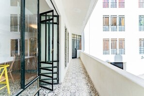 A narrow corridor with patterned flooring, a glass door, and a view of a building with multiple windows. - Vibrant Condo in Roma Norte Walk to Museums & Eats (Mexico City)