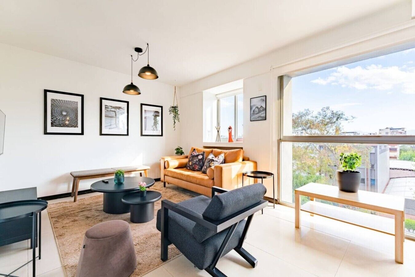 A modern living room with a sofa, coffee table, and chairs, a balcony with a view, and framed artwork on the walls.