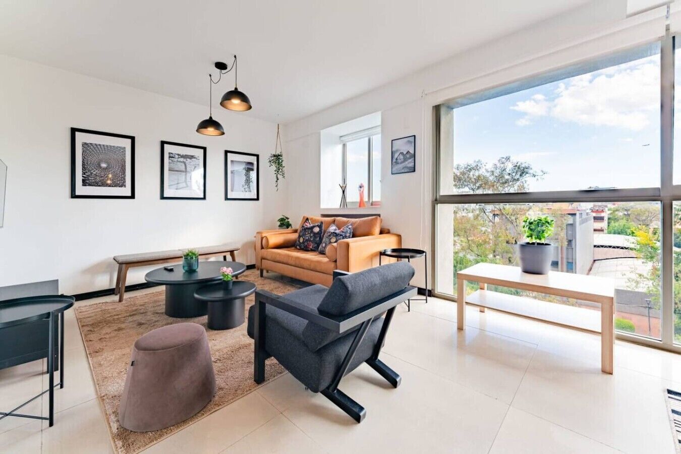 Un salon moderne comprenant un canapé, une table basse, un pouf et une grande fenêtre donnant sur l’extérieur.