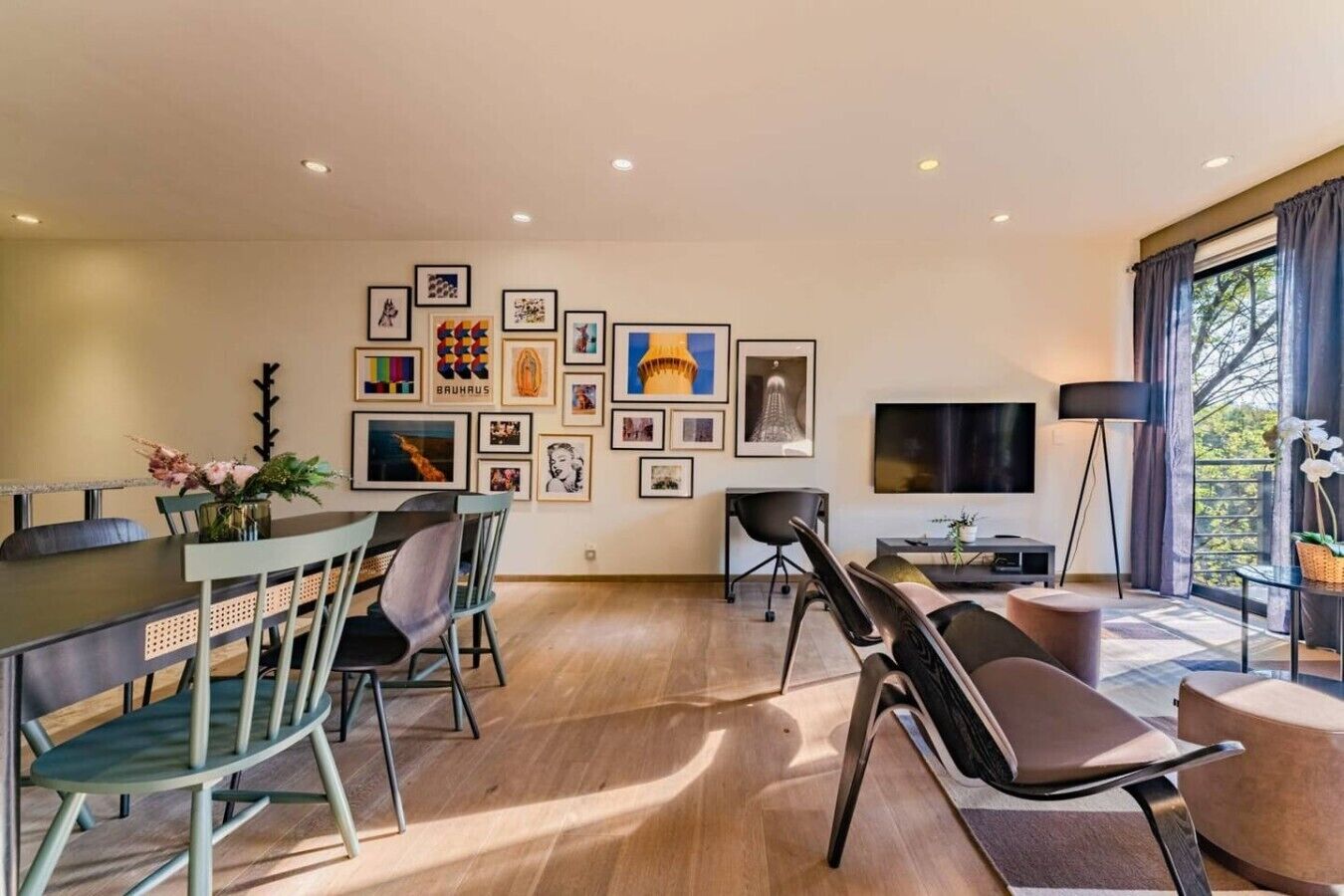 A modern living room with a dining area, a flat-screen TV, and a large window with curtains.