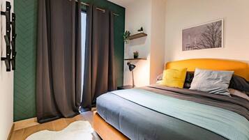 A bedroom with a bed, curtains, a nightstand, a lamp, a shelf with plants, and a painting on the wall.
