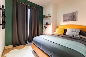A bedroom with a bed, curtains, a nightstand, a lamp, a shelf with plants, and a painting on the wall. - Roma Norte Condo: Balcony, Parking & City Views (Mexico City)