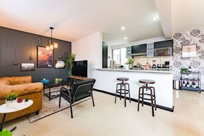 A modern living room with a sofa, a coffee table, and a TV. There is a kitchen area with a bar and stools. - Roma Norte Condo with City Views & Workspace (Mexico City)