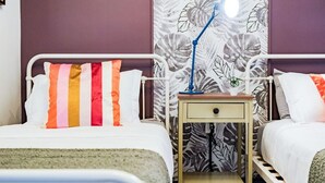 Hotellihuone, jossa on kaksi sänkyä, yöpöytä lampun kanssa ja kukkakuviollinen verho.