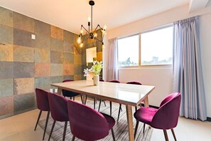 A dining area with a table and chairs, a modern chandelier, and a large window with curtains. - Roma Norte Condo with City Views & Workspace (Mexico City)