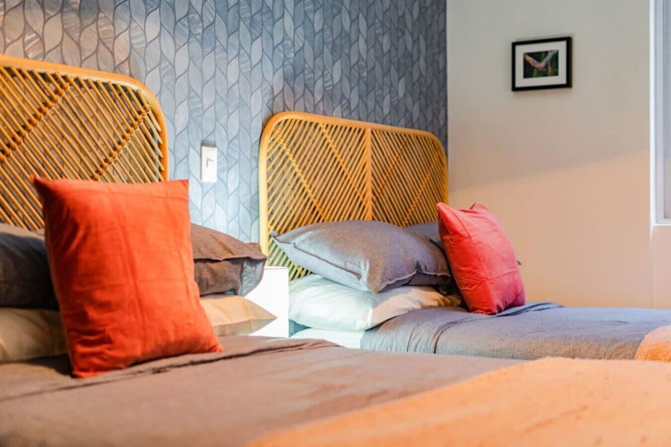 Une chambre d’hôtel avec deux lits, chacun doté d’une tête de lit en osier, et un mur orné d’un motif.
