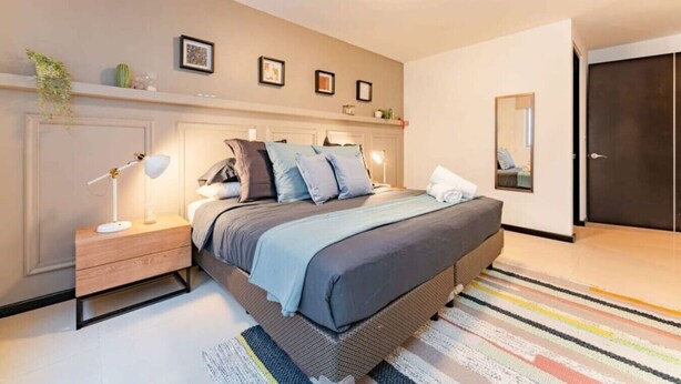 Quarto moderno com cama, mesas de cabeceira, um criado-mudo, um espelho e uma porta.