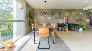 Uma sala de jantar moderna com uma mesa grande, cadeiras e vista para o verde lá fora.