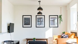 Uma sala de estar moderna com televisão de tela plana, uma mesa de centro redonda, um sofá e três obras de arte emolduradas na parede.