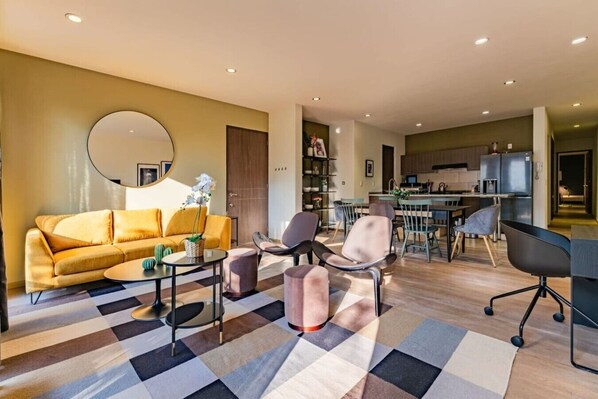 A modern living room with a sofa, chairs, a coffee table, and a dining area with a kitchen in the background. - Spacious Roma Norte Stay: Balcony & Workspace (Mexico City)
