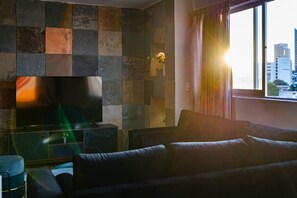 Ein Wohnzimmer mit Flachbildfernseher, einer Couch und einem Fenster mit Blick auf die Stadt.