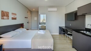 A modern hotel room with a bed, a desk, a chair, a TV, and a kitchen area. - Studio in Historic Center Near Santa Casa Tco0712 (Porto Alegre)