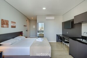Ein modernes Hotelzimmer mit Bett, Schreibtisch, Stuhl, Fernseher und einer Küchenzeile.