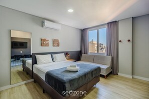 A modern hotel room with a large bed, a sofa, a TV, and a city view. - Studio w/ Pool Near Redencao Park Tco1216 (Porto Alegre)