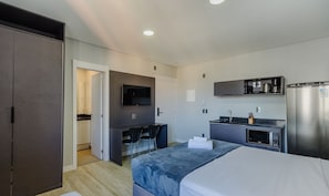 A compact hotel room with a bed, a desk, a kitchenette, and a TV. - Studio w/ Pool Near Redencao Park Tco1216 (Porto Alegre)